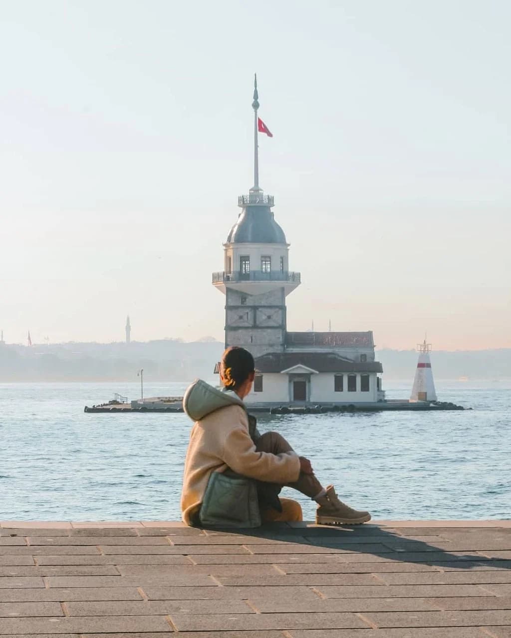 Woman sitting by the Bosphorus with Maiden's Tower in the distance